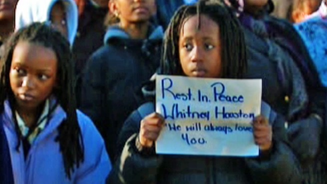 Elementary school students at the Whitney Houston Academy in New Jersey pay tribute to the late music icon by visiting her childhood home, standing silent while a flag hangs at half-staff and releasing a bouquet of white balloons into the air.