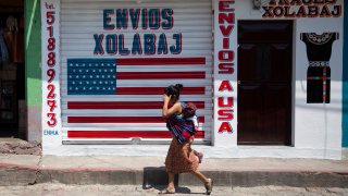 a woman carrying a child walks past a closed courier business featuring a U.S. flag and the Spanish phrase: "Deliveries to U.S.A"
