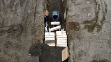 Workers wearing personal protective equipment bury bodies in a trench on Hart Island, Thursday, April 9, 2020, in the Bronx