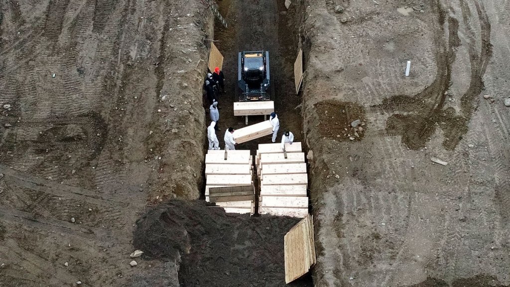 Workers wearing personal protective equipment bury bodies in a trench on Hart Island, Thursday, April 9, 2020, in the Bronx