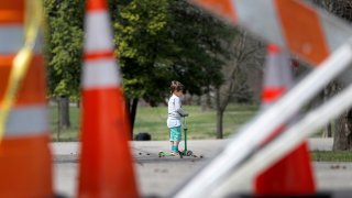 a child rides a scooter past barricades at an entrance to Tower Grove Park in St. Louis.