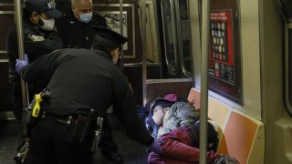officers approach a person sleeping on a subway train