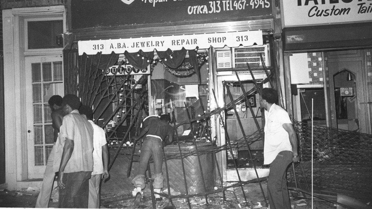 A man reaches through the shattered windows of a looted jewelry store on Utica Ave., in Brooklyn during New York City's electrical power failure, Thursday, July 14, 1977. Looters ripped the steel gratings away from the windows. (AP Photo)