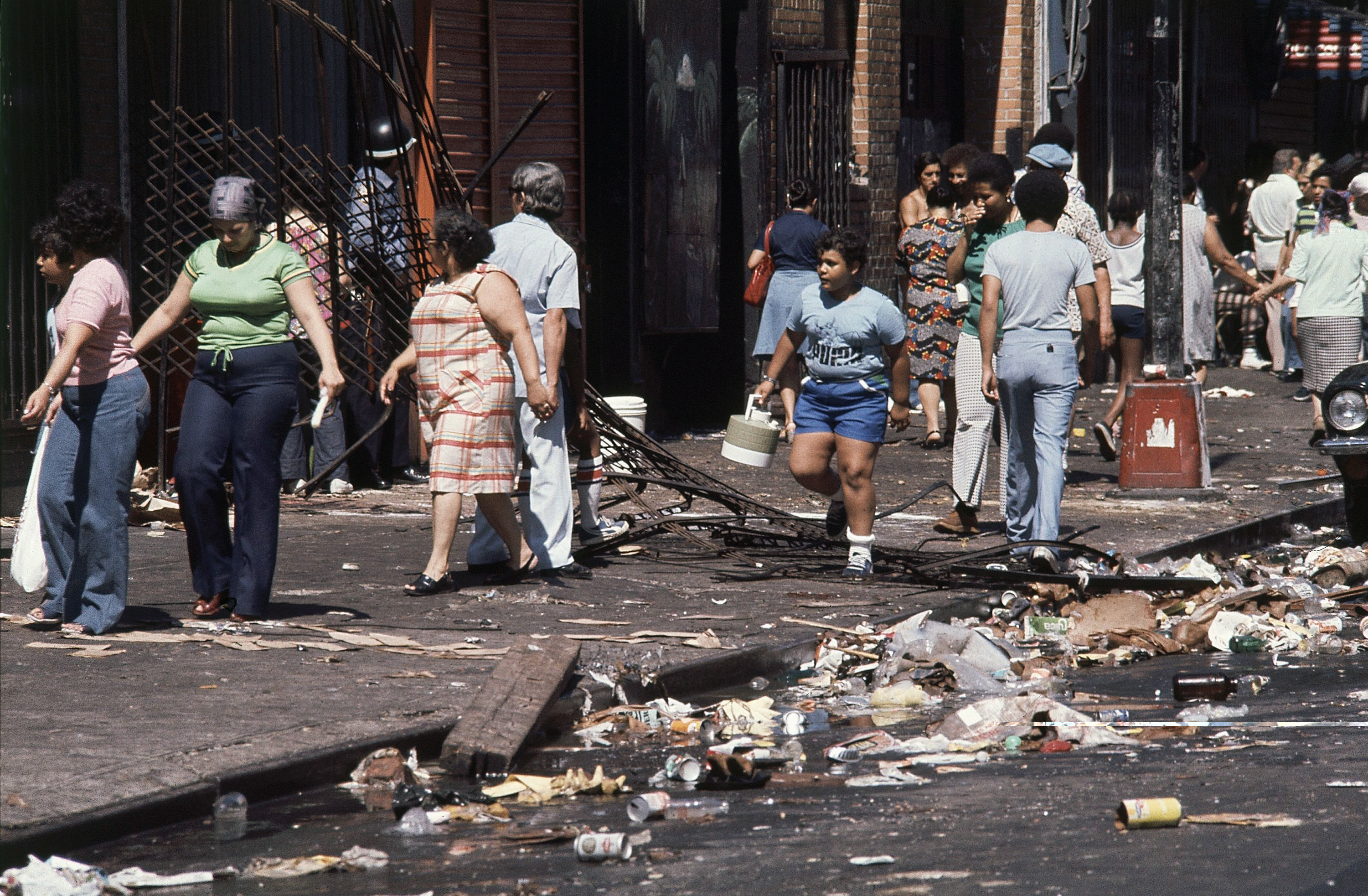 People walk amid debris following looting at 110th St. and Third Avenue in upper Manhattan, New York City after the power failure, July 14, 1977. (AP Photo/Ira Schwarz)
