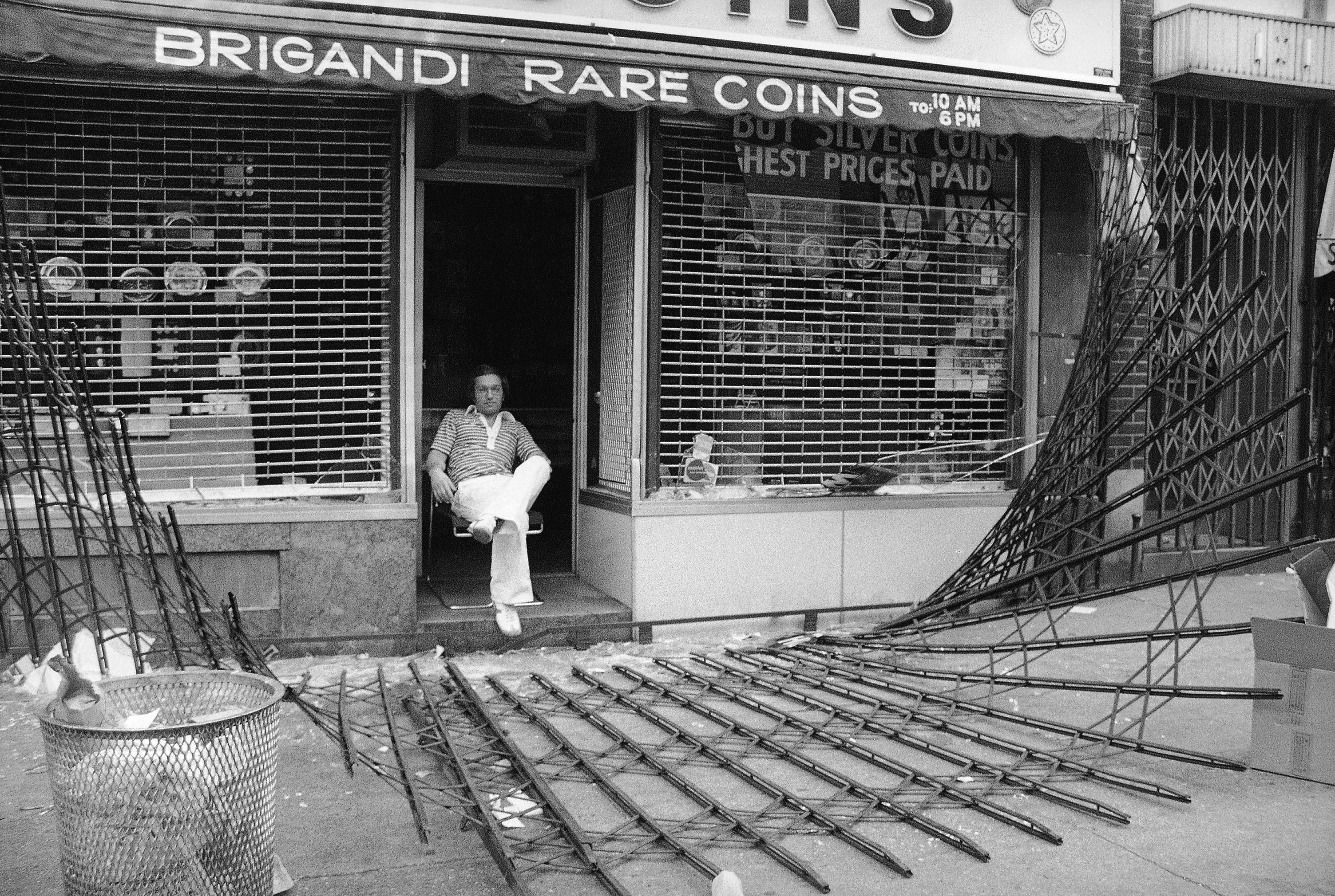 The owner of midtown Manhattan coin shop sits disconsolately in his doorway in New York on Thursday, July 14, 1977.