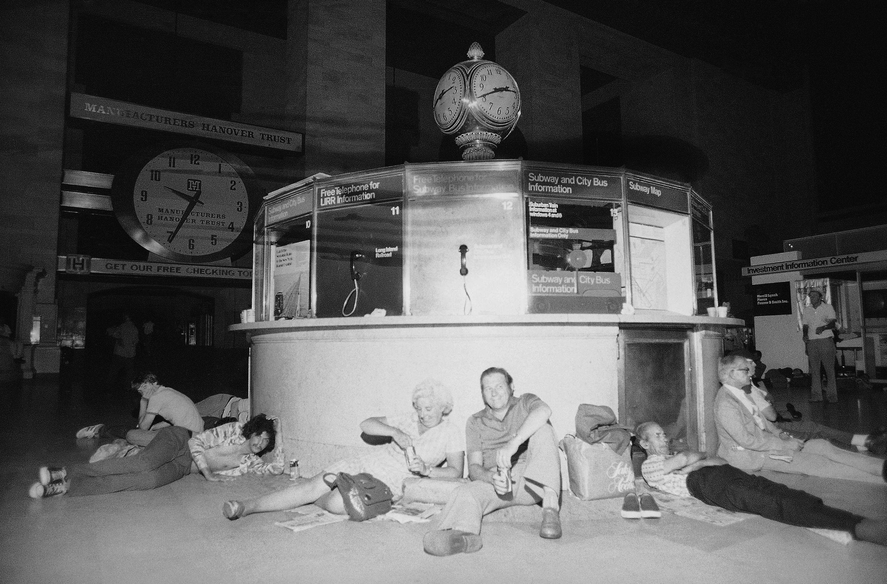 People huddle against the information kiosk in New York's Grand Central Station, July 14, 1977 after being stranded by a power failure in the city.