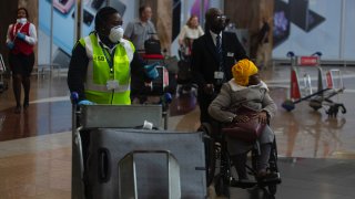 An elderly passenger arrives in a wheelchair   at Johannesburg’s O.R. Tambo International Airport, Monday, March 16, 2020 a day after President Cyril Ramaphosa declared a national state of disaster Sunday saying that the country has 61 cases, including local transmission of COVID-19, and he expected the number to increase dramatically. For most people, the new coronavirus causes only mild or moderate symptoms. For some it can cause more severe illness, especially in older adults and people with existing health problems.  (AP Photo/Denis Farrell)