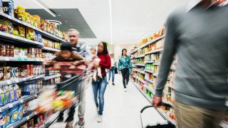 A busy supermarket aisle with various customers buying groceries.