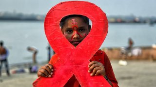 A young girl holds a placard of a red ribbon during the World AIDS Day