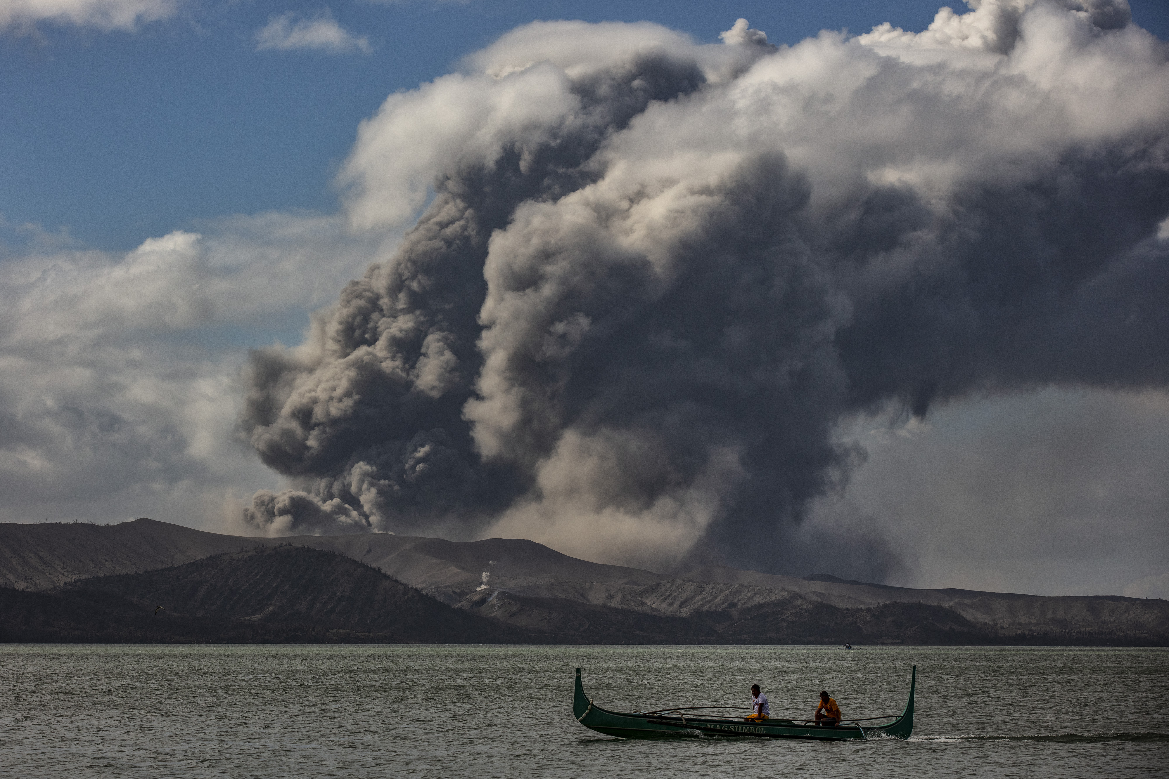 A fishing boat sails along a lake as the Taal volcano erupts, Jan. 14, 2020, in Talisay, Philippines.