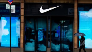 A pedestrian holding an umbrella passes in front of a closed Nike Inc. store in the SoHo neighborhood of New York, U.S., on Tuesday, March 17, 2020.