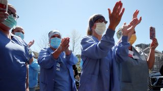In this April 23, 2020, file photo, hospital staff members cheer for emergency department nurse Debbie Buonopane as she departs Brigham And Women’s Hospital in Boston, Mass.