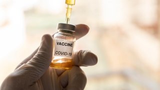 Cropped hand wearing a nitrile glove holding a COVID-19 vaccine vial and a syringe.