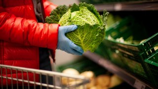 Woman picking out savoy cabbage at the supermarket, wearing protective gloves