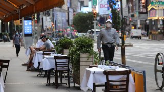 A person walks by tables placed outside for outdoor dining at a Serafina restaurant in midtown