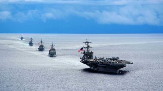 Photograph of the aircraft carrier USS Theodore Roosevelt leading a formation of ships from Carrier Strike Group during a maneuvering exercise in 2014.
