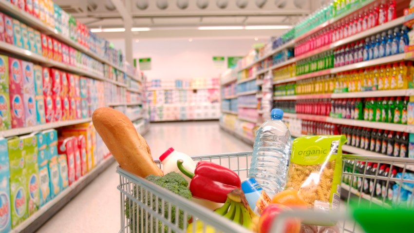 Supermarket cart filled with vegetables in aisle.
