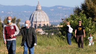 People walk at the 'Pineto' park with St. Peter's basilica in the background on the first day after Italy lifted its lockdown, May 4, 2020, in Rome. Italy was the first country to impose a nationwide lockdown to stem the transmission of the coronavirus, and its restaurants, theaters and many other businesses remain closed.