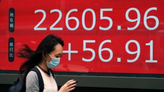 In this June 24, 2020, file photo, a woman walks past an electronic stock board showing Japan's Nikkei 225 index at a securities firm in Tokyo.