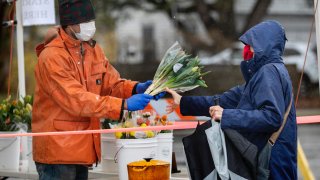 David Baecher sells flowers to a customer at a farmer’s market Friday, May 1, 2020, in Brunswick, Maine. Gov. Janet Mills is requiring that people wear masks in public to help prevent the spread of the coronavirus as part of her business reopening plan.