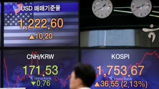 In this March 31, 2020, file photo, a currency trader walks by the screens showing the Korea Composite Stock Price Index (KOSPI), right, and the foreign exchange rate between U.S. dollar and South Korean won, left top, at the foreign exchange dealing room in Seoul, South Korea.