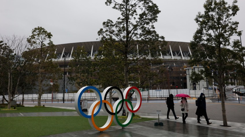 In this March 4, 2020, file photo, people walk past the Olympic rings near the New National Stadium in Tokyo.