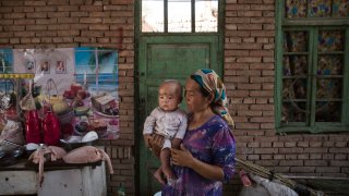 In this Sept. 12, 2016, file photo, a Uyghur woman holds a child in her home as they prepare food during the Corban Festival in Turpan County, in the far western Xinjiang province, China.
