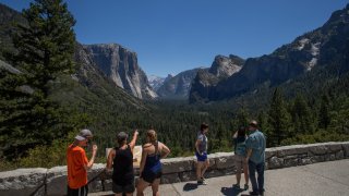 Visitors walk to the Tunnel View lookout in Yosemite Valley at Yosemite National Park, California on July 08, 2020. - After closing for 2½ months because of the coronavirus pandemic, the wildlife is taking over of areas used by the public. The park is open with limited services and facilities to those with day-use reservations, reservations for in-park lodging or camping, and wilderness or Half Dome permits.