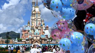 Visitors wearing face masks look at the Castle of Magical Dreams at Hong Kong Disneyland
