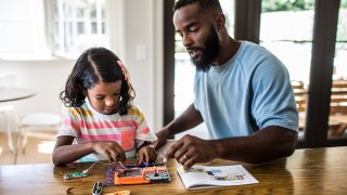 A photo of a father and daughter working on a science project at home.