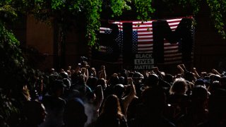 Protesters raise their fists in solidarity as they listen to a speaker during a night of protest against racial injustice on July 31, 2020 in Portland, Oregon, as the letters BLM for 'Black Lives Matter' are seen on a flag of the United States that hangs upside down. - US federal officers will stay in the protest-wracked city of Portland until local law enforcement officials finish a "cleanup of anarchists and agitators," the US President said.