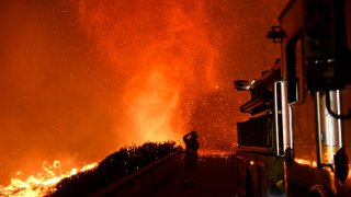 A firefighter observes a fire tornado from an overpass above the 101 freeway on December 6, 2017 in Ventura, California