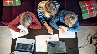 Mother helping sons with homeschooling at home during COVID-19 pandemic.