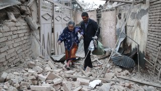 A man helps a woman get over the rubble left by shellfire