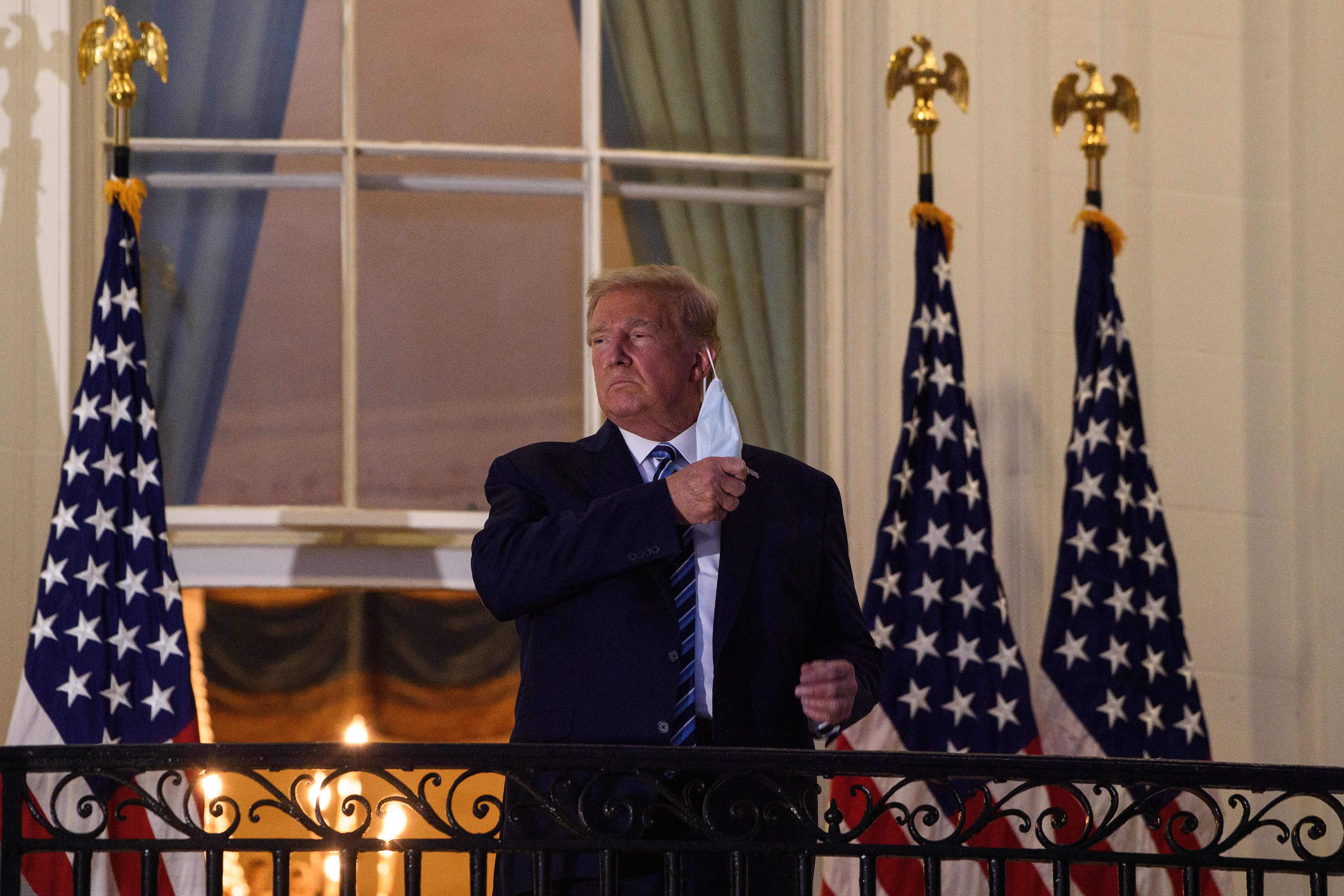 President Donald Trump takes off his face mask as he arrives at the White House upon his return from Walter Reed Medical Center, where he underwent treatment for Covid-19, in Washington, D.C, on Oct. 5, 2020.