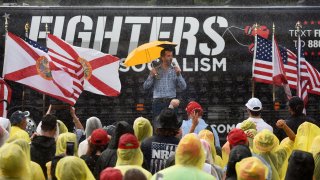 Donald Trump Jr speaks while holding an umbrella to supporters wearing ponchos during a rain shower at a Fighters Against Socialism campaign rally in support of his father, U.S. President Donald Trump. UFC fighter Jorge Masvidal also spoke at the event.