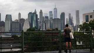 Person looks out at the Manhattan skyline in a Brooklyn neighborhood.