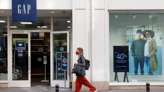 A woman wearing a protective face mask walks past a GAP store on October 22, 2020 in Paris, Franc