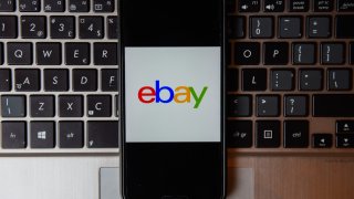 In this photo illustration an Ebay logo seen displayed on a smartphone with a laptop keyboard on the background.