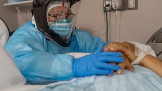 A medical staff member Susan Paradela pauses for a moment as she places her hands on a a deceased patient’s hands before put the patient into a body bag in the COVID-19 intensive care unit (ICU) at the United Memorial Medical Center on December 6, 2020 in Houston, Texas.