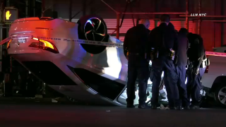 A white sedan rests upside down on an East Harlem street after its driver lost control and flipped the vehicle