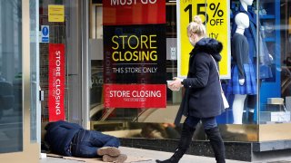 A pedestrian wearing a face mask delivers food to a homeless person sleeping in the entrance of a shop, closed due to coronavirus restrictions, in central London on December 23, 2020.