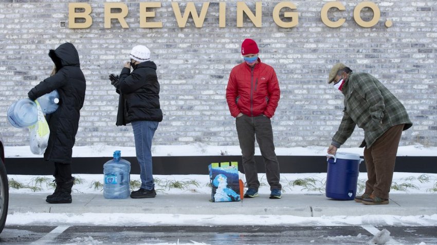 Tina Hall, left to right, Susana Sosa, Jim Sefcik and Chris Sosa wait in line to fill up their containers with water at Meanwhile Brewing Company in Austin, Texas, on Friday, Feb. 19, 2021, during a citywide boil water notice caused by the winter storm. The brewery gave away all 4,000 gallons of their water to people in need on Thursday and Friday. (Jay Janner /Austin American-Statesman via AP)