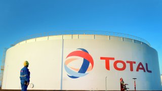 An employee of the ‘Total’ oil refinery stands in front of a large tank with the company’s logo in Leuna, Germany.