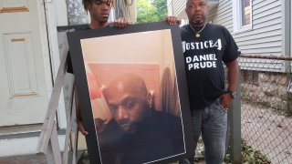 FILE - In this Sept. 3, 2020, file photo, Joe Prude, brother of Daniel Prude, right, and his son Armin, stand with a picture of Daniel Prude in Rochester, N.Y. Daniel Prude, 41, suffocated after police in Rochester put a "spit hood" over his head while he was being taken into custody. He died March 30, after he was taken off life support, seven days after the encounter with police. The independent investigator leading a probe of the city's handling of Prude's death says the ex-police chief is refusing to cooperate.