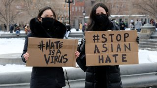 Protestors hold signs that read "hate is a virus" and "stop Asian hate" at rally