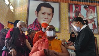 A health worker inoculates a dose of a COVID-19 coronavirus vaccine to a Buddhist monk sitting in front of a portrait of Bhutan's King Jigme Khesar Namgyel Wangchuck (top C) during the first day of vaccination in Bhutan, at Lungtenzampa Middle Secondary school in Thimphu on March 27, 2021.
