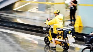 A Meituan food delivery worker on motorcycle in the rain in Futian Central Business District, Shenzhen, China.