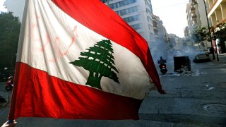 An anti-government demonstrator waves the national flag as they block the street, with burning garbage dumpsters, in front of Lebanon’s central bank in the capital Beirut on March 16, 2021, during a protest against the deteriorating economic situation.