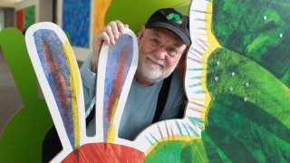 This file photo shows Eric Carle stand with a large cutout of the iconic image from his children's book, "The Very Hungry Caterpillar," at his museum in Amherst, Mass.